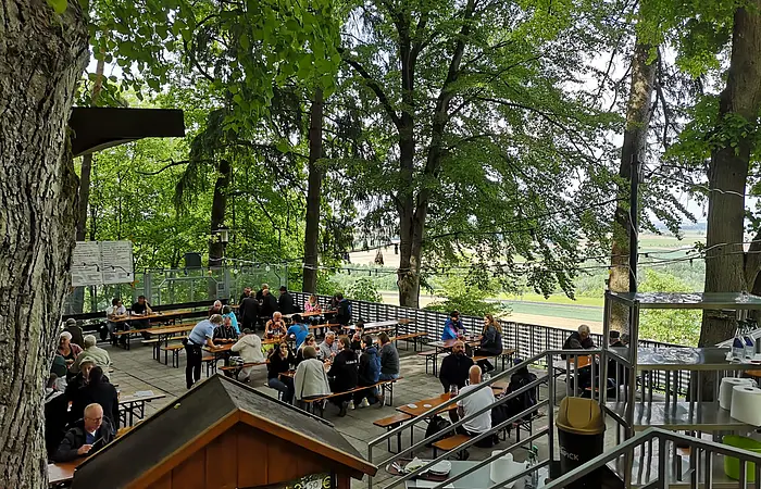 Von der oberen Terrasse hat man den Blick auf die untere, man sieht Gäste an den Tischen und einen Teil des großen, alten Baumbestandes