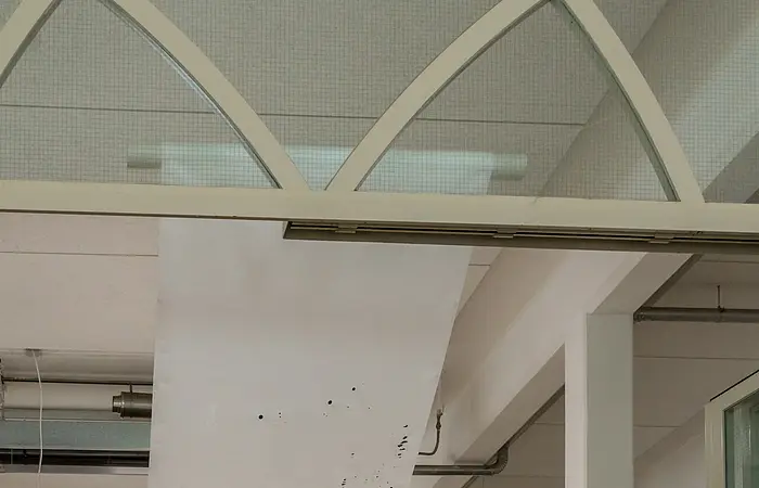 Innenraum einer Galerie mit weißen Stellwänden und abstrakten Bildern, Steinboden und Bogenfenstern.