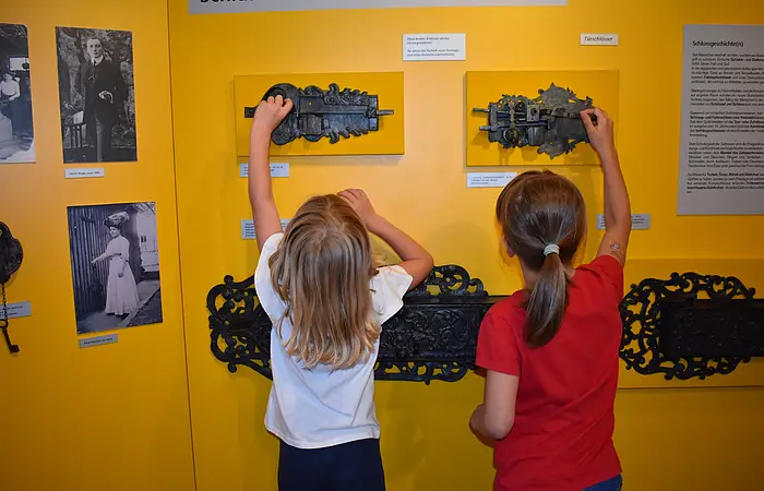Zwei Kinder probieren alte, an der Wand befestigte Schlösser aus