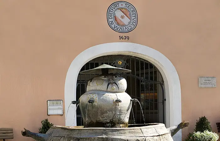 Chinesenbrunnen vorm Rathaus im Mittelpunkt, ganz vorne links Blumen.