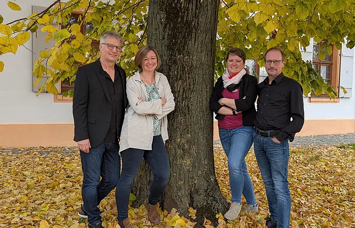Vier Sänger*innen stehen auf Herbstlaub unter einem Baum