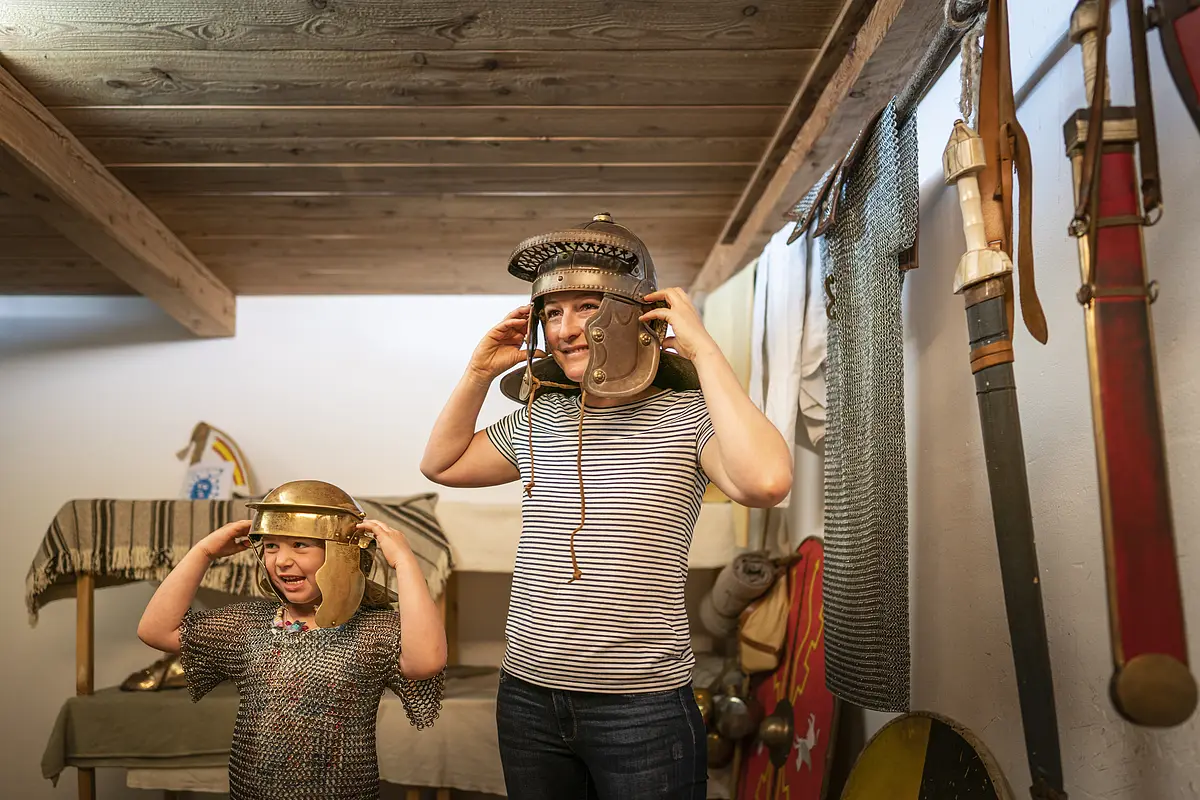 Frau und Kind probieren antike römische Helme und Kettenhemden in einem Museum an.