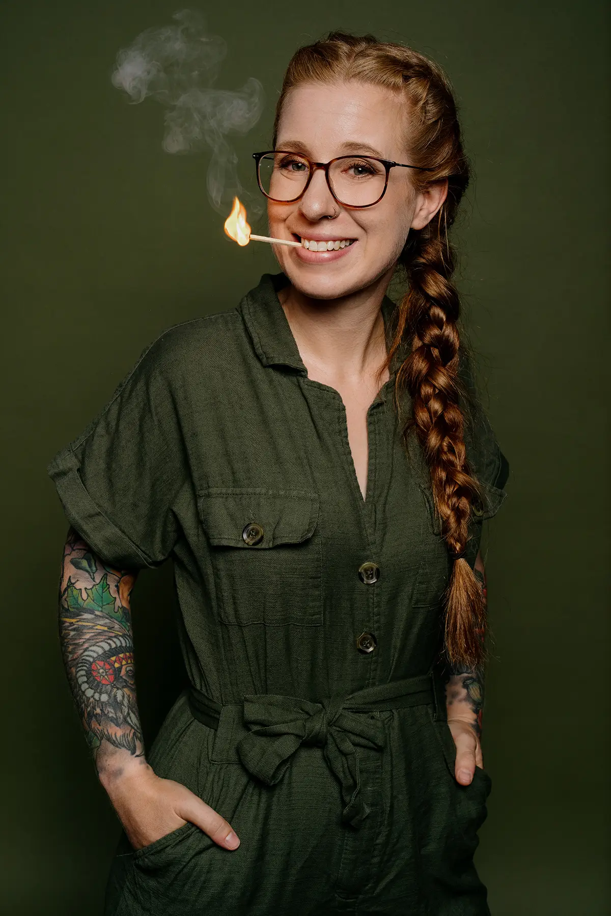 Sara Brandhuber "A scheena Schmarrn" Künstlerin im grünen Jumpsuit vor grünem Hintergrund mit Streichholz im Mund