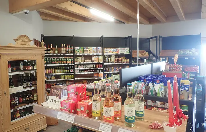 Innenansicht eines kleinen Lebensmittelgeschäfts mit Regalen, Holzmöbeln und verschiedenen Produkten.